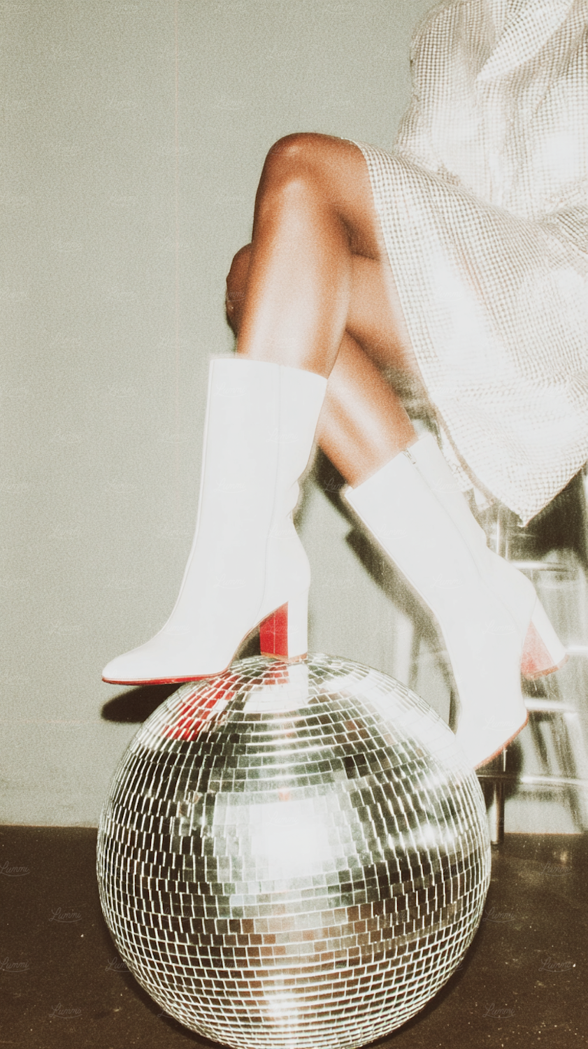 White boots with red soles resting on a mirrored disco ball beside a sequinned outfit
